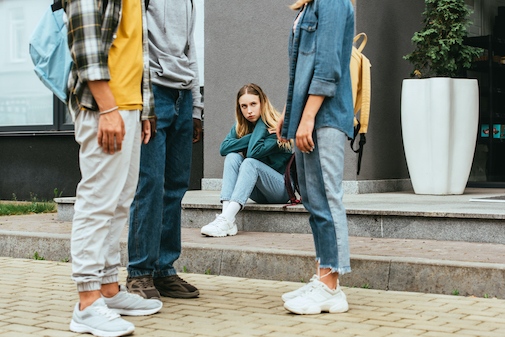A sad teenage girl sitting down, looking at three friends