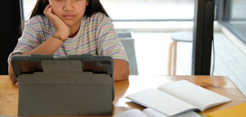 En flicka sitter vid ett skrivbord och tittar på en digital läsplatta