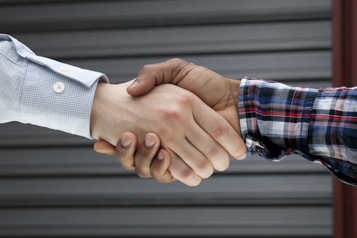 A handshake between one person with a white shirt and one with a checkered shirt