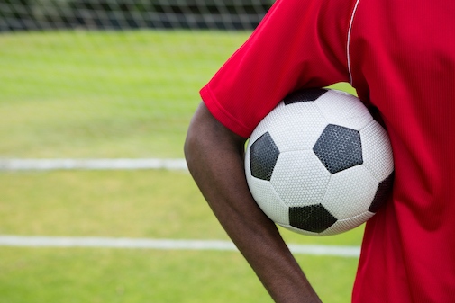 En mörkhyad fotbollsspelare håller i en fotboll på en fotbollsplan