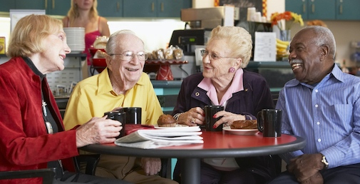 Fyra äldre personer runt ett bord skrattar och dricker kaffe
