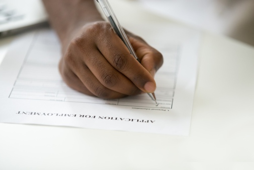 A dark-skinned hand writing a job application